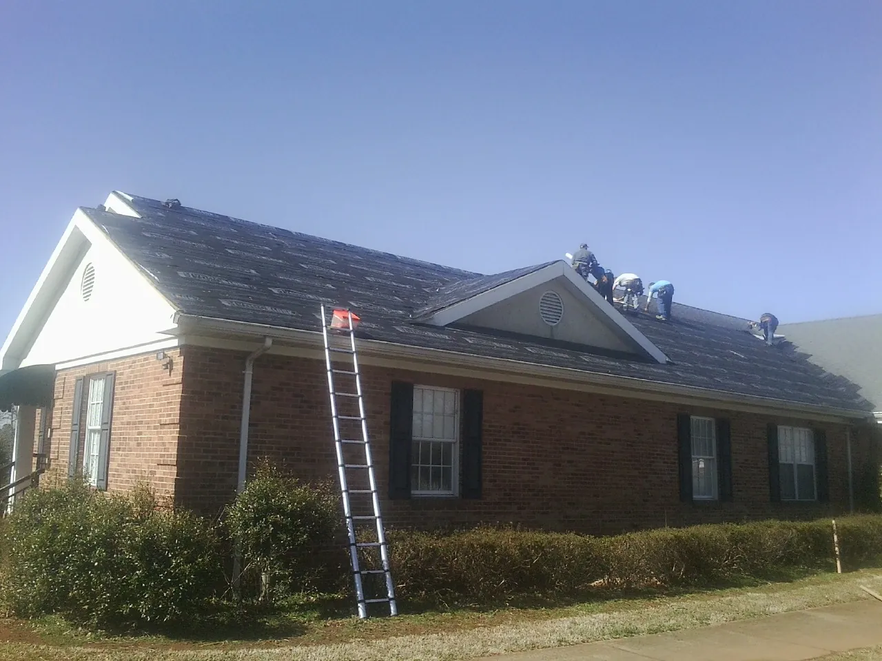 Crew tearing shingles off a brick ranch roof with a ladder set — Emergency Roof Repair work by our crew in Lewis