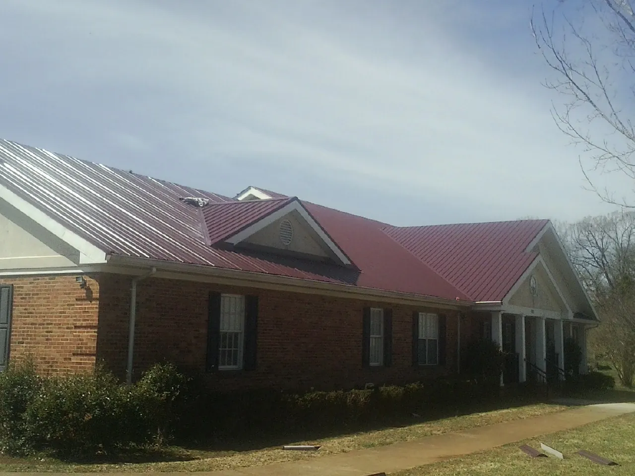 Red metal roof with gabled entries on a long brick building, from a Hail Damage Roof Repair job in Lewis