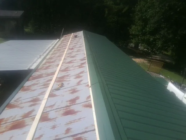 Old rusted panels beside newly installed green metal roofing — Wind Damage Roof Repair by Roofing Brothers in Lewis