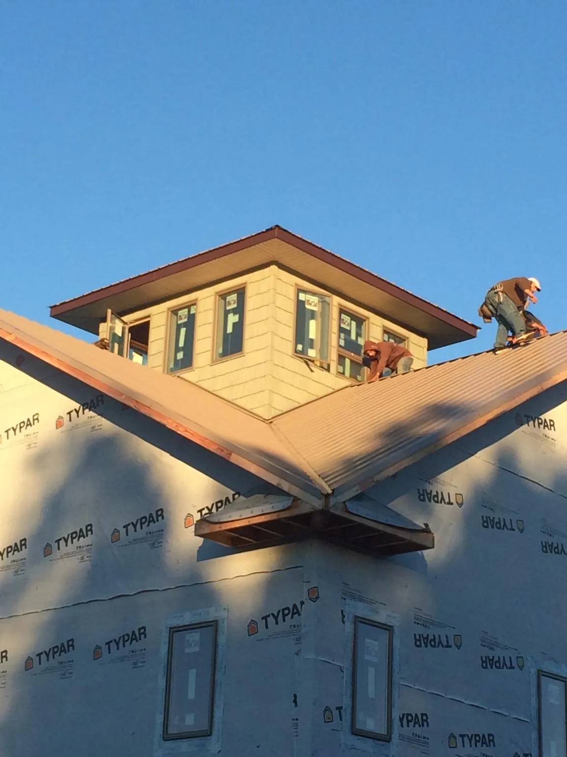 Roofers working around a rooftop cupola on a new metal roof at sunset — Roof Waterproofing in Lewis by Roofing Brothers